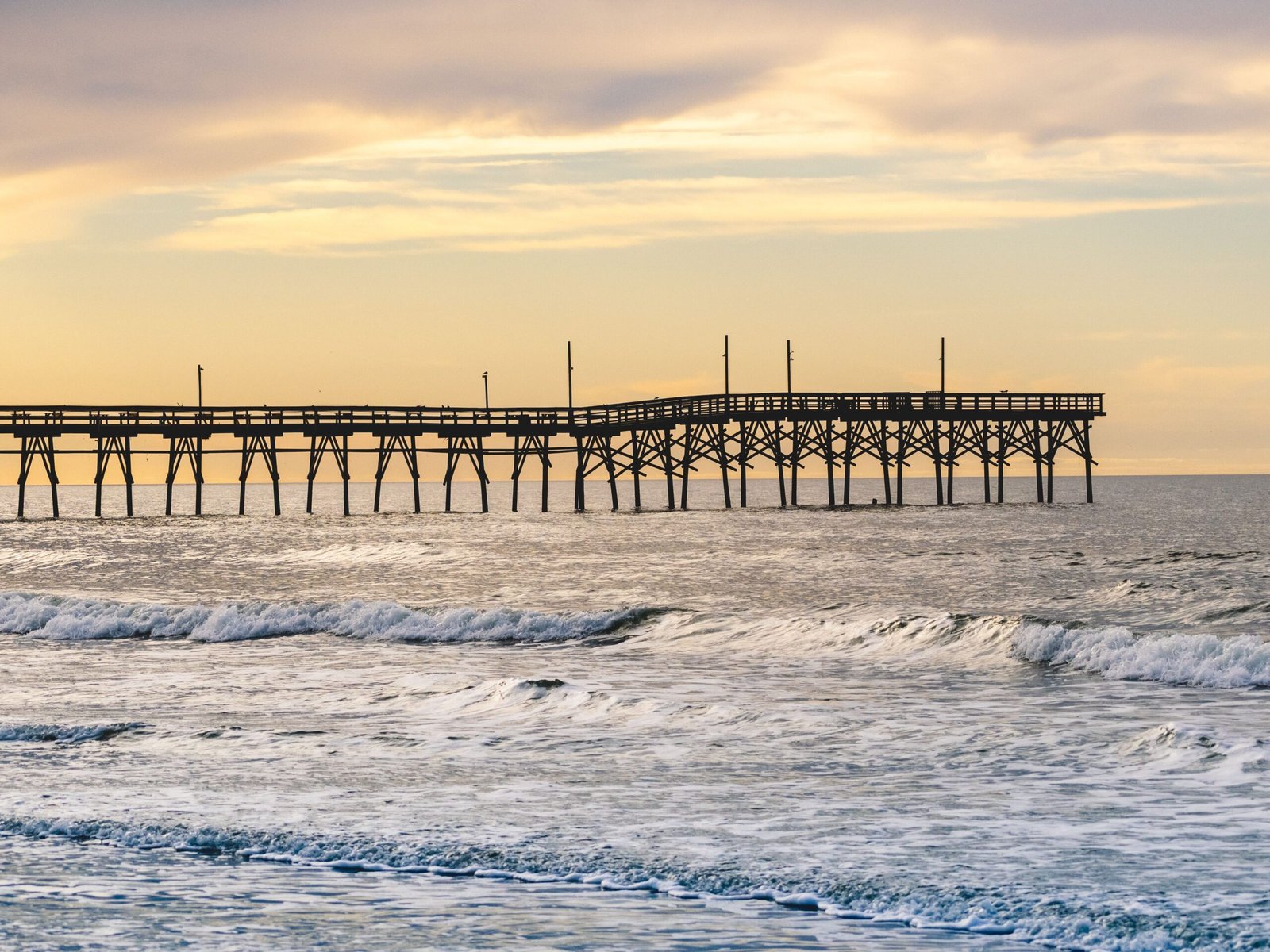 Home Peaceful evening at Sunset Beach Pier, North Carolina with gentle waves and a colorful sky.